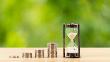 Coin stack and hourglass on wooden desk  on green tree background, time for saving concept