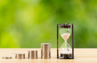 Coin stack and hourglass on wooden desk  on green tree background, time for saving concept
